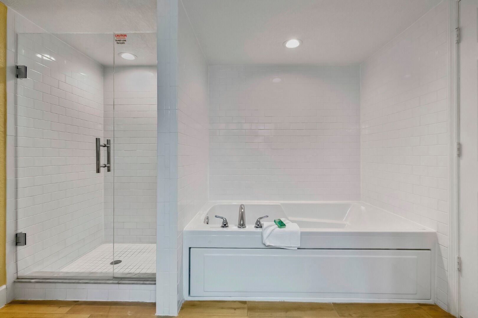Un baño moderno con ducha acristalada, una bañera blanca con una toalla y suelo de madera.