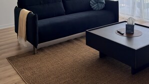 Un soggiorno moderno con un divano nero, un tavolino da caffè, una ventola a soffitto e un'ampia finestra con tende leggere.