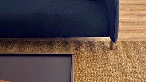 Un soggiorno moderno con un divano scuro, un quadro astratto blu e un tappeto testurizzato.