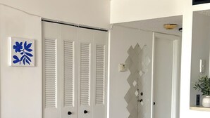 Un corridoio con pavimento in legno, pareti bianche e una porta bianca con persiane.