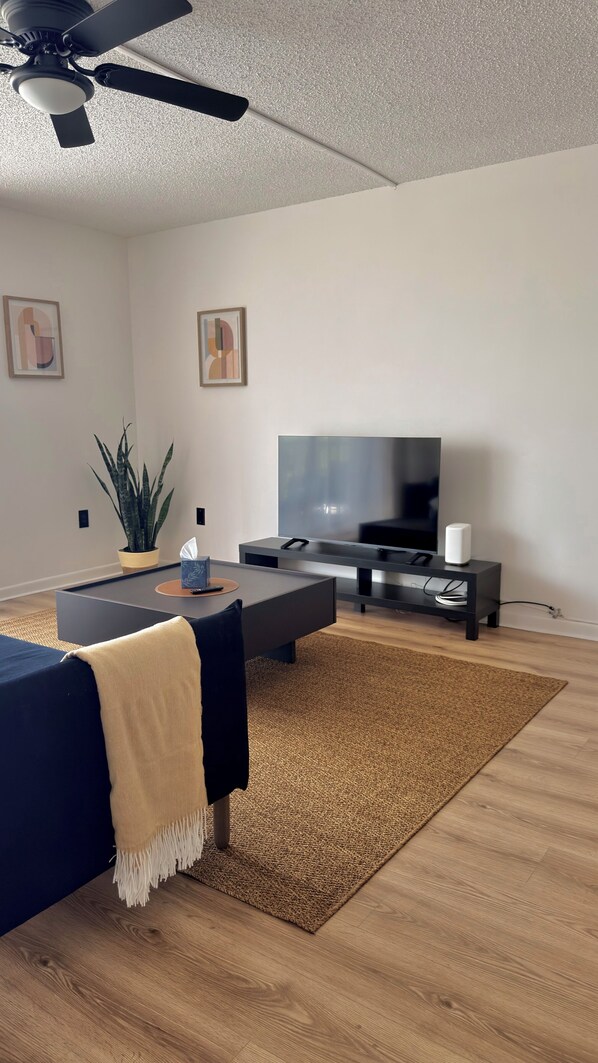 Una sala de estar moderna con televisión de pantalla plana, ventilador de techo, planta en maceta y una mesita de centro.