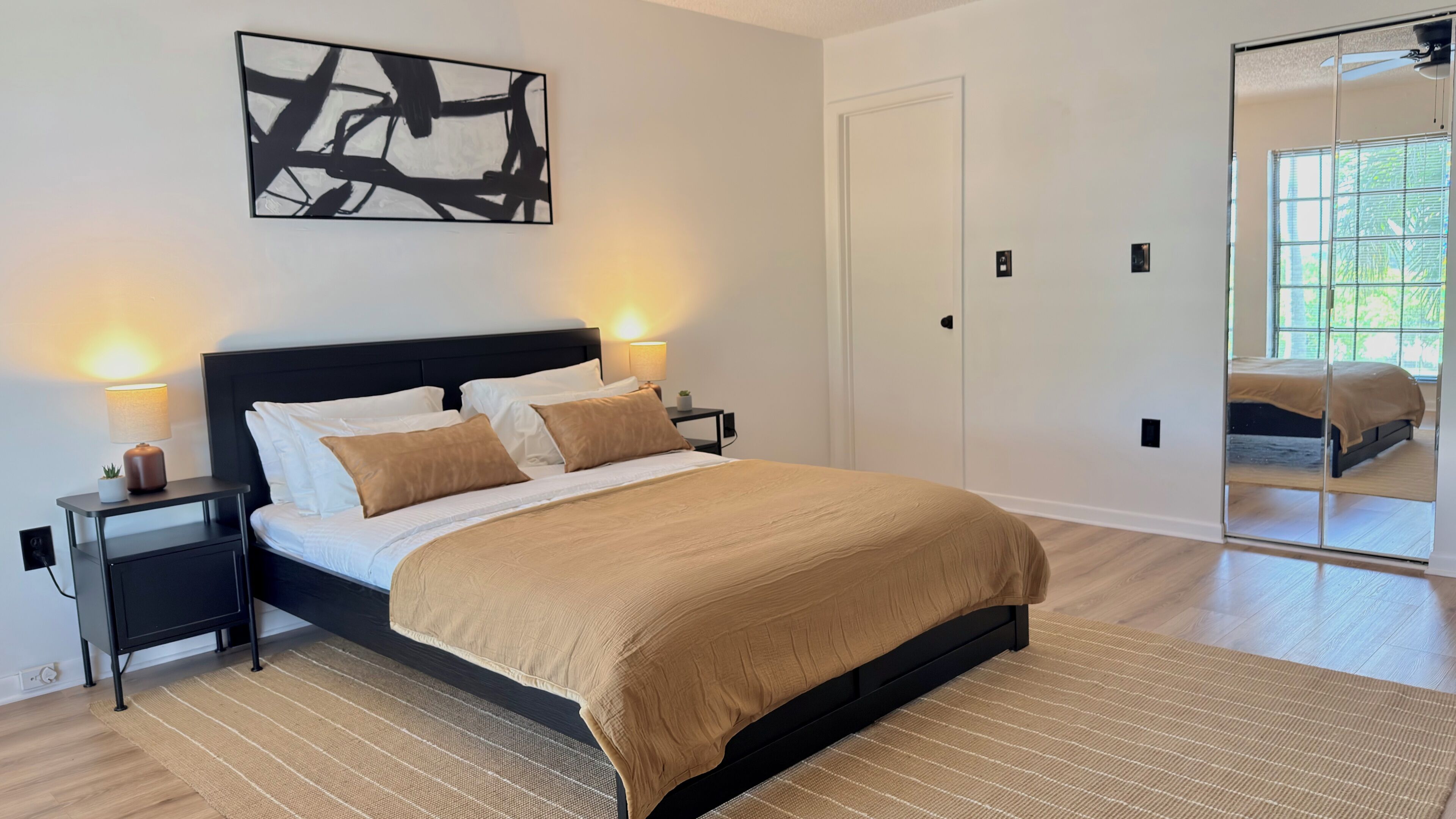 Ein modernes Schlafzimmer mit einem großen Bett, Nachttischlampen, einem Wandbild und einem Spiegel.