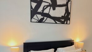 A neatly made bed with a black headboard, two bedside tables with lamps, and a large abstract painting on the wall. - Cozy 1-bedroom apartment in adorable Lauderhill with AC (Lauderhill)