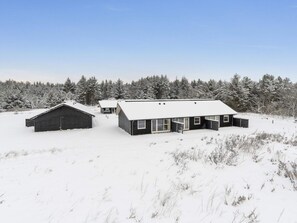 Schneebedeckte Landschaft mit zwei modernen Gebäuden, eines mit Satteldach und das andere mit Flachdach, umgeben von einem Wald.