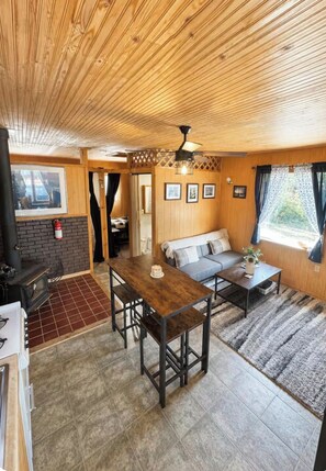 A cozy cabin interior with a wooden ceiling, a fireplace, a dining table, and a sofa. - Rustic Red Retreat & Sauna (Talkeetna)