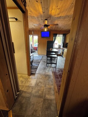 Un intérieur en bois avec un ventilateur de plafond, un téléviseur, un coin repas et une cuisine.