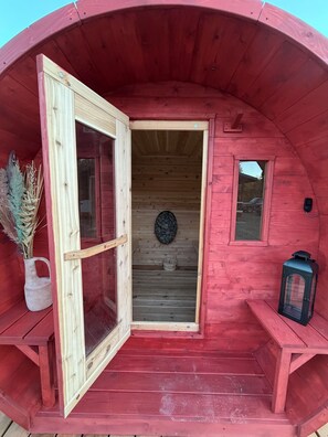 A red wooden structure with an open door, a small table, a lantern, and a decorative item on the wall. - Rustic Red Retreat & Sauna (Talkeetna)