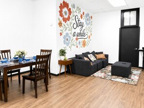 Un salon moderne comprenant un coin repas, une porte noire et un mur orné d’une fresque florale.