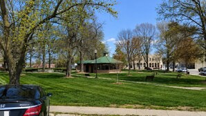A park with a gazebo, benches, and a building with arched windows. - Firefly Lofts (Cameron)