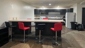 A kitchen with a bar area, black and red bar stools, a refrigerator, and a trash bin.