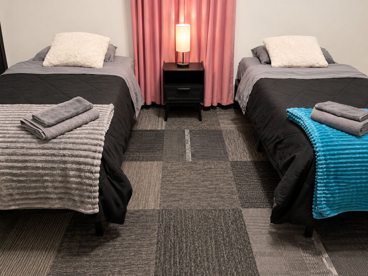 A hotel room with two beds, a nightstand with a lamp, and a patterned carpet.