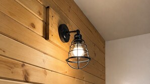 A wooden wall with a bed, a wall-mounted light fixture, and a power outlet.