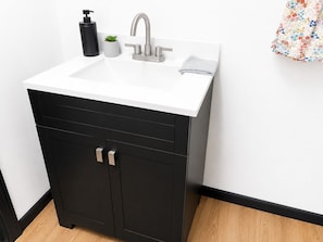 Une salle de bain avec un lavabo blanc, un meuble noir et une petite plante en pot.