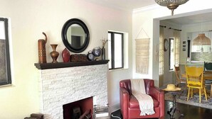 A living room with a fireplace, a red leather sofa, a dining area with a yellow chair, and a hanging light fixture. - 2 Bedroom House in the Heart of Miami + Parking (Miami)