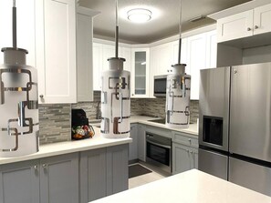 Una cucina moderna con elettrodomestici in acciaio inossidabile, mobili grigi e illuminazione a sospensione.