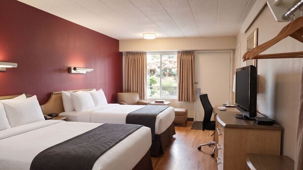 Habitación de hotel con dos camas, un escritorio con computadora, un televisor y una ventana con cortinas.