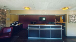 Un hall de hotel con mostrador de recepción, televisor, chimenea y una silla roja.