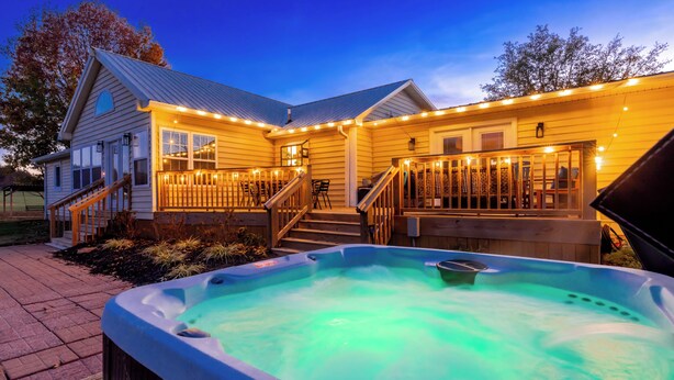 Een huis met een jacuzzi, een houten terras en lichtjes.