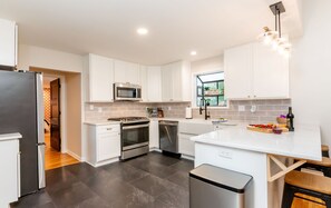 Eine moderne Küche mit weißen Schränken, Edelstahlgeräten, einer zentralen Kochinsel und einem Fenster mit Blick.