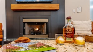Een open haard met een boek getiteld 'Bardstown' en een fles Elijah Craig whisky op een tafel.