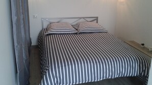 Sängyssä on raidallinen vuodevaatesetti, metallinen pääty ja kaksi seinään kiinnitettyä valaisinta.