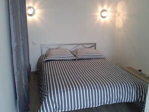 Ein Bett mit gestreifter Bettwäsche, einem Metall-Kopfteil und zwei Wandleuchten.