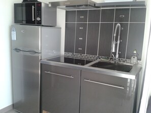 Eine kleine Küche mit Kühlschrank, Mikrowelle und Spüle aus Edelstahl.