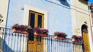 A building with a balcony, a window with a flower box, and a door. - La Casetta Azzurra (Aci Castello)