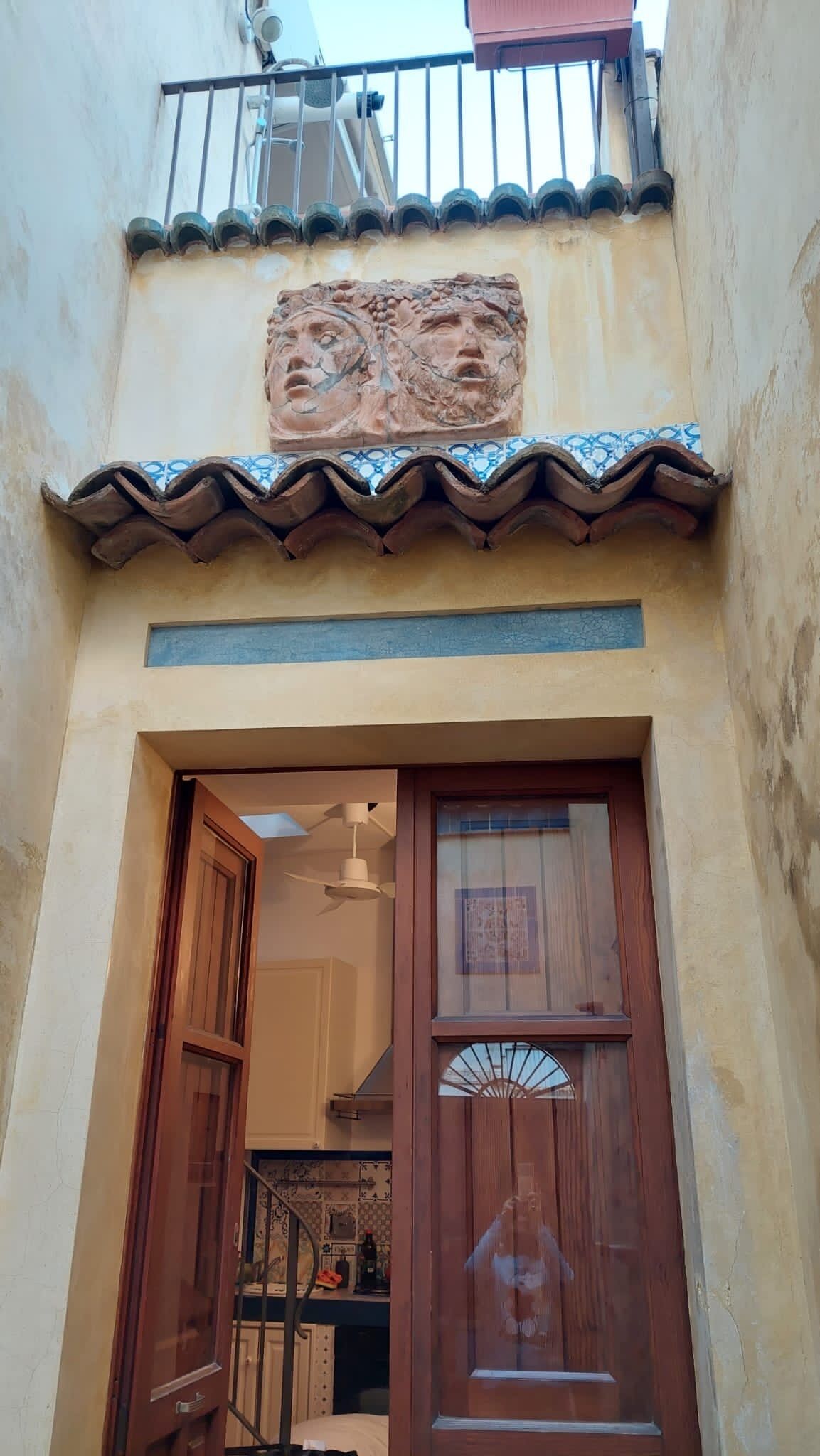 Une entrée d’immeuble avec une porte en bois, un petit balcon doté d’une balustrade et une sculpture ornementale en pierre au-dessus de la porte.