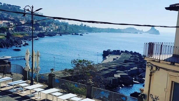 A coastal view with a patio area, outdoor seating, and a view of the sea. - La Casetta Azzurra (Aci Castello)