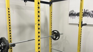 Un gimnasio con una estructura amarilla para sentadillas, discos de pesas y un banco.