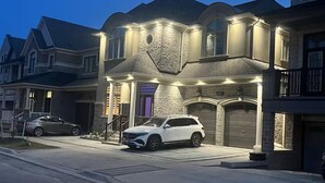 Una casa de dos pisos con fachada de piedra, un garaje y una entrada para coches con dos vehículos estacionados.