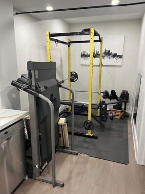 A home gym with a treadmill, weight bench, and a squat rack. - Designer 4BR Basement Suite – Oakville
Entire basement in Oakville, Canada (Oakville)