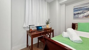 Habitación de hotel con un escritorio de madera, una computadora portátil, una colcha verde y un cuadro en la pared.