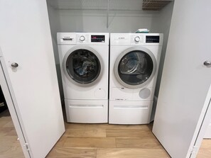 A compact laundry room with two white Bosch washing machines, a wooden floor, and a white door. - Stunning brand new South Austin condo 2 mi from DT (Austin)