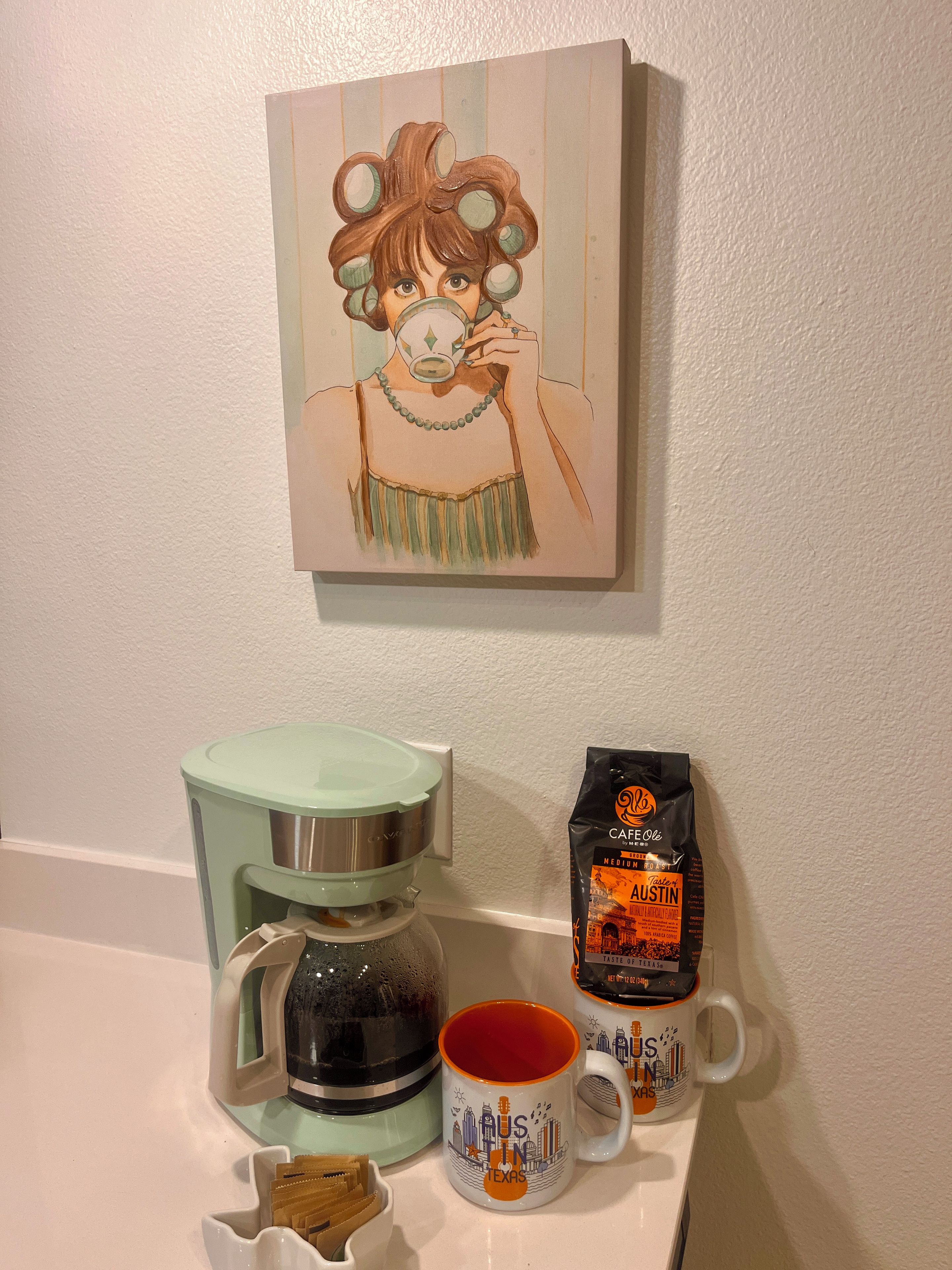 Una cafetera, una taza y un paquete de café sobre una encimera.