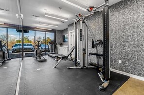 Un gimnasio con equipamiento de ejercicio, un ventanal y vista a vehículos estacionados.