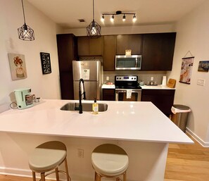 Una cocina moderna con una isla central, electrodomésticos de acero inoxidable e iluminación colgante.