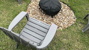 En patio med fire Adirondack-stole, et rundt bord og et bålsted med sort låg.