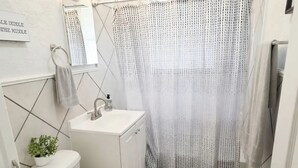 Et badeværelse med toilet, håndvask og bruseforhæng.