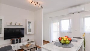 Un soggiorno moderno con una TV a schermo piatto, un divano, un tavolino da caffè, un'area pranzo con una ciotola di frutta e un lampadario.