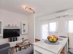 A modern living room with a flat-screen TV, a sofa, a coffee table, a dining area with a fruit bowl, and a ceiling light fixture. - One Bedroom Apartment with Terrace and Sea View (Sukosan)