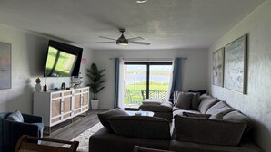 A living room with a sofa, chairs, a TV, a ceiling fan, a plant, and a view of a body of water through a window. - Waterfront Flagler Beach Retreat I 2 King Beds I 2 Full Baths I Kayaks (Flagler Beach)