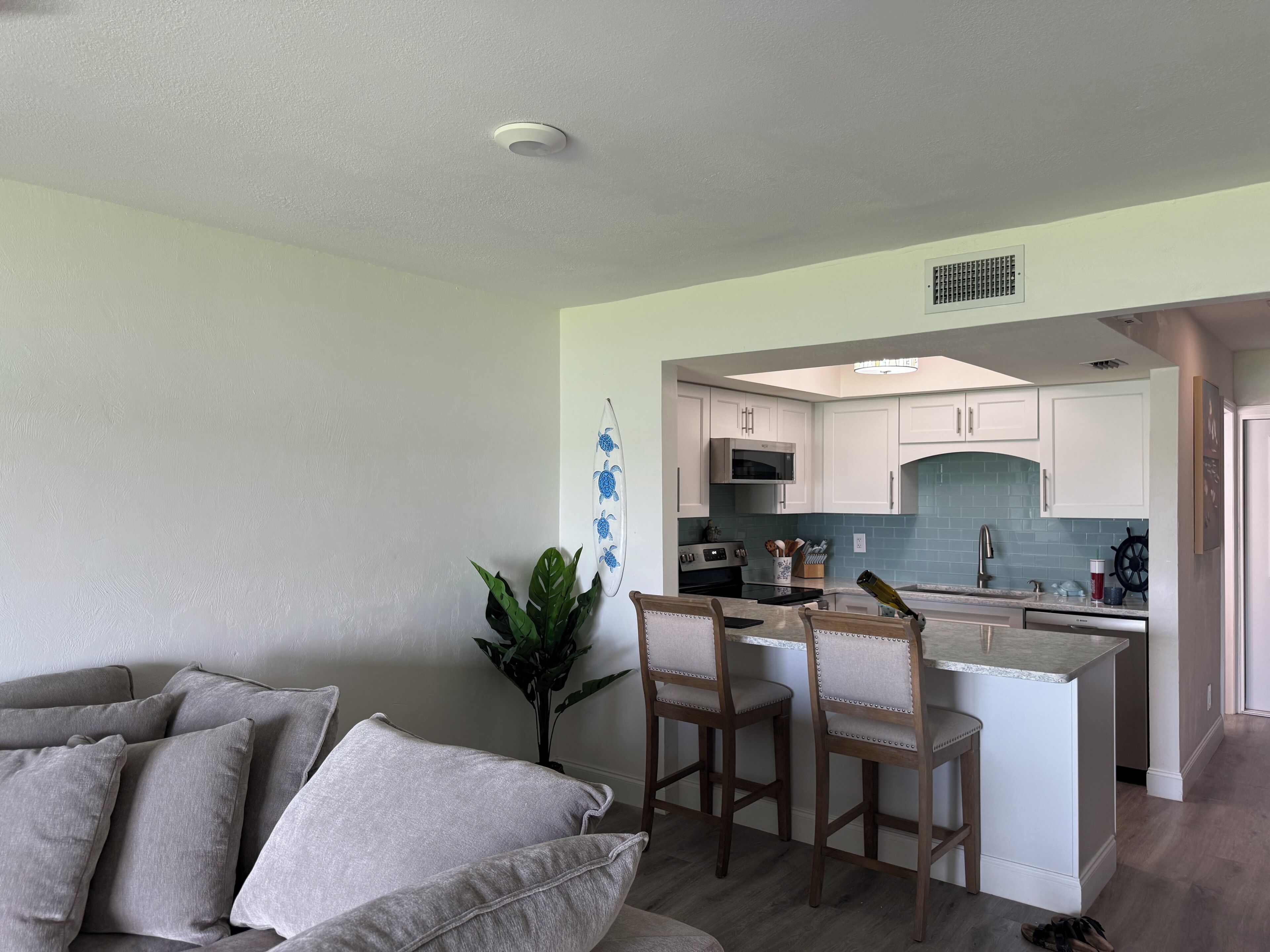 A modern kitchen with white cabinets, a central island, and a dining area with a grey sofa and two bar stools.