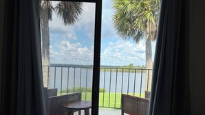 A view through a sliding door to a balcony with a table and chairs, overlooking a body of water and palm trees. - Waterfront Flagler Beach Retreat I 2 King Beds I 2 Full Baths I Kayaks (Flagler Beach)