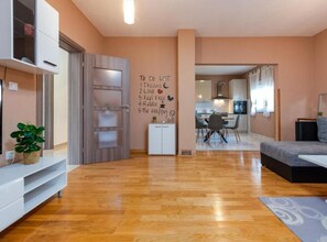 A modern living room with a wooden floor, a sofa, a dining area with a table and chairs, and a kitchen in the background. - Two Bedroom Apartment with Terrace (Sukosan)