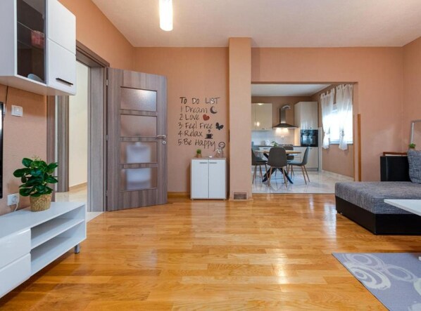 A modern living room with a wooden floor, a sofa, a dining area with a table and chairs, and a kitchen in the background. - Two Bedroom Apartment with Terrace (Sukosan)