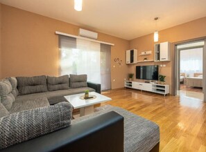 A modern living room with a sectional sofa, a coffee table, a TV, and a built-in entertainment unit. - Two Bedroom Apartment with Terrace (Sukosan)