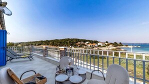 A balcony with a table set for dining, chairs, and a view of a coastal town. - Villa with pool and sea view (Pasman)