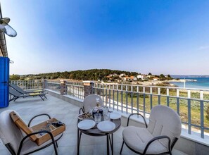 A balcony with a table set for dining, chairs, and a view of a coastal town. - Villa with pool and sea view (Pasman)